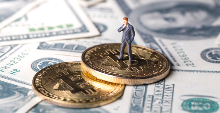 Ein Miniatur-Mann steht auf einem Haufen Bitcoins und US-Dollars