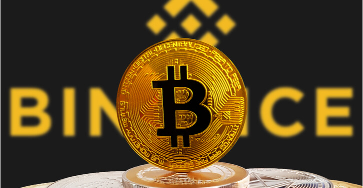BTC auf einem Stapel von Krypto-Coins mit Binance-Logo im Hintergrund