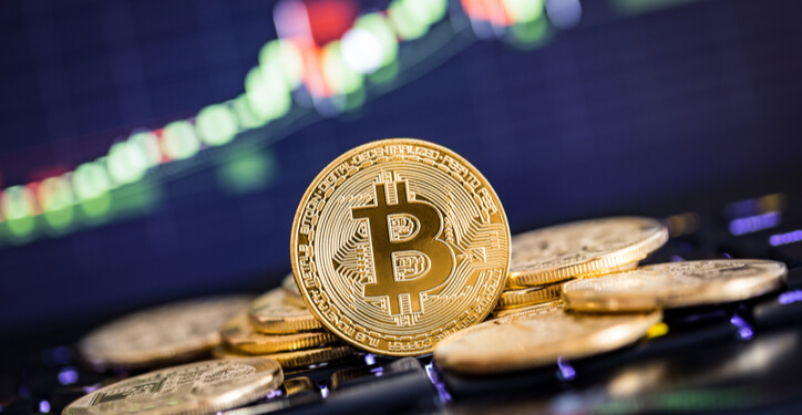 Bitcoins auf einer Tastatur vor einem Trading-Chart